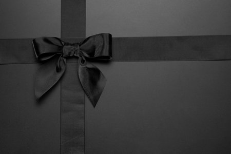 Black ribbon with bow on black background. Black and white photo.の写真素材