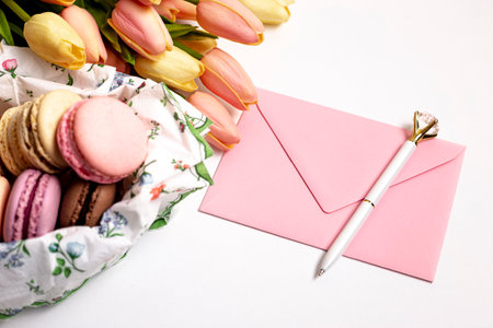 Bouquet of tulips, macaroons and envelope on white background