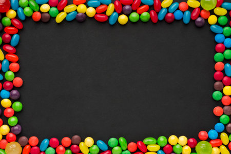 Frame of multicolored candies on black background with copy space
