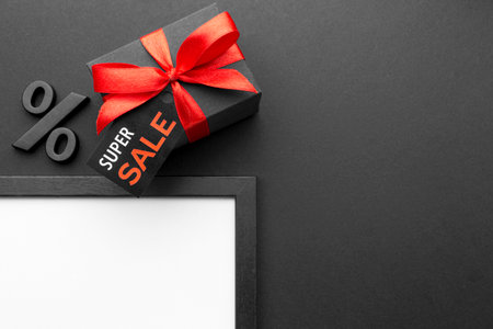Black gift box with red ribbon and sale sign on black background.