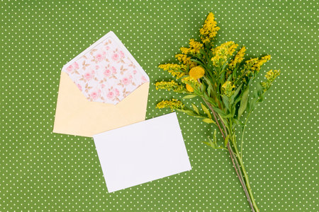 Beautiful bouquet of yellow wildflowers and envelope on green polka dot backgroundの写真素材
