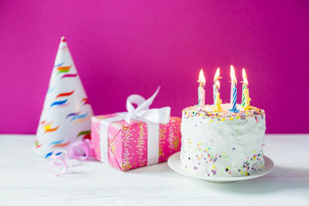 Birthday cake with candles, gifts and party hat on pink backgroundの写真素材