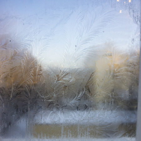Winter sunrise in winter frozen window evening scene. Frozen winter window view. Ice patterns on frozen window in the cityの写真素材