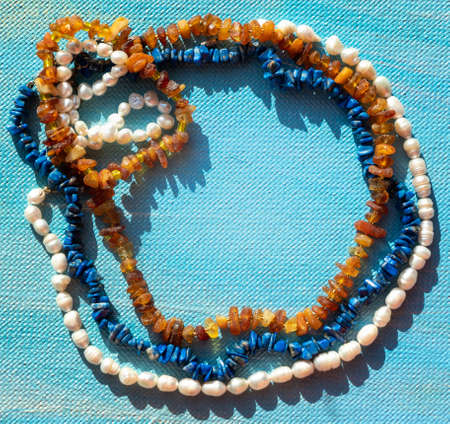 A set of sea natural jewelry. Space for the text. Coral amber pearl and bone jewelry on a blue background. Top view. High quality photoの写真素材