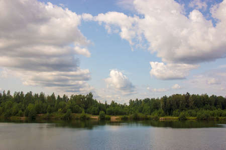 Summer landscape with a beautiful wild lake with clear water, cloudy sky and green fir forest.