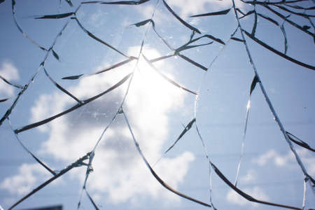 Broken glass with cracks on blue sky background. Close up view of broken glass textureの写真素材