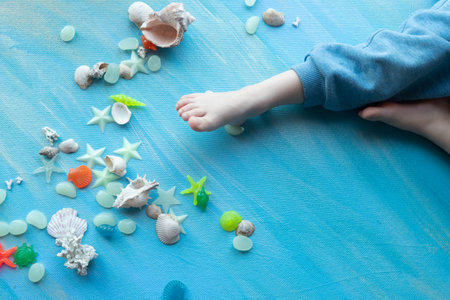 baby feet on Seashells summer background. Many different seashells, starfish on a background of blue...