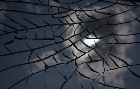 Broken glass with cracks on blue sky background. Close up view of broken glass textureの写真素材