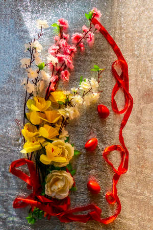 Easter card with painted red Easter eggs and flowers on a silver background. Decorated with painted artificial spring flowers and a scarlet ribbon.の写真素材