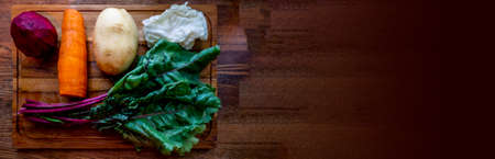 A board with ingredients for cooking delicious borscht on a wooden background. Cabbage, potatoes,...
