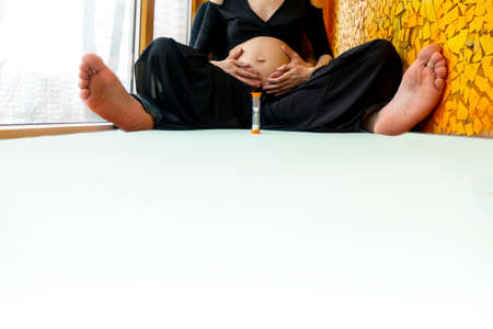 pregnancy, love, family and people concept - pregnant woman and her husband making hand heart gesture on her belly sitting in the lotus position. high quality photoの写真素材