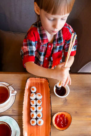 Little cute little boy eating sushi in a cafe, concept of eating. the boy in the restaurant eats sushi, dumbly holding chopsticks. View from aboveHigh quality photoの写真素材