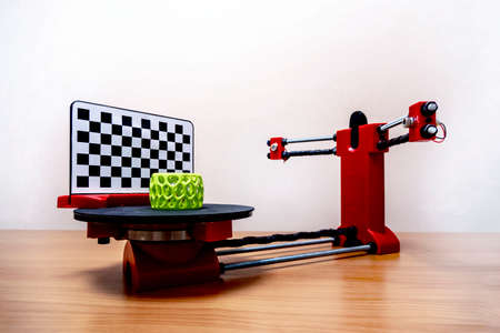 a small desktop 3D scanner scans a green object printed on a 3D printer