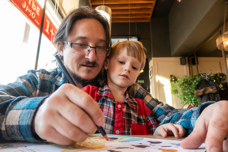 a child with his father in a restaurant draws a coloring book, waiting for cookingの写真素材