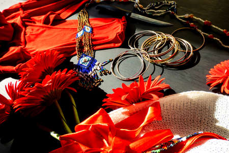 flat lay of a fashionable look from red and white accessories on a black background. Scarlet dress and white hat with a ribbon, jewelry made of beads and small stones, light jingling braceletsの写真素材