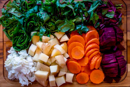 A board with ingredients for cooking delicious borscht on a wooden background. Cabbage, potatoes, carrots, beets with tops. Step by step process of slicing vegetables for beetroot soup High quality photoの写真素材