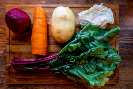A board with ingredients for cooking delicious borscht on a wooden background. Cabbage, potatoes, carrots, beets with tops. Step by step process of slicing vegetables for beetroot soup High quality photoの写真素材