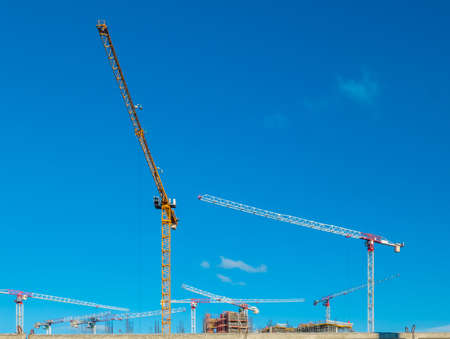 Construction cranes work on creation site against blue sky background. Bottom view of industrial...