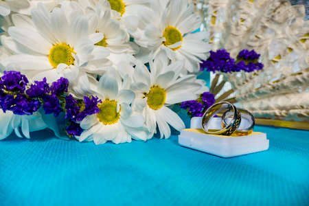 Wedding bouquet of bride. wedding card with original rings in a white box, a bouquet of white chrysanthemums or daisies and a white lace fan on a blue backgroundの写真素材