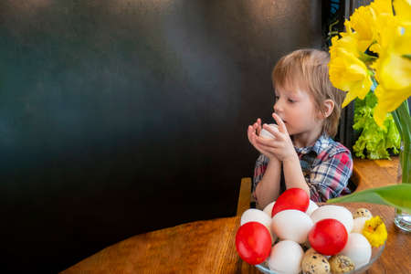 Preparation for Easter: a child plays with painted eggs in the kitchen among fresh greenery and...