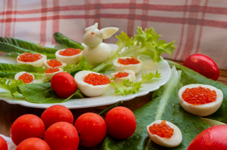 background of red caviar on dark wooden surface. edible egg rabbit figurine for decorating dishes easter dish decorated with red painted Easter eggs, cherry tomatoes and lettuce leavesの写真素材