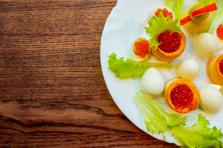 background of red caviar on dsrk wooden surface. tartlets with red caviar. edible egg yolk chicken figurine for decorating dishesの写真素材