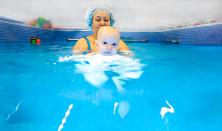 Adorable baby girl enjoying swimming in a pool with her mother early development class for infants teaching children to swim and dive. Swimming instructor doing exercises with a small child in the pool . High quality photoの写真素材