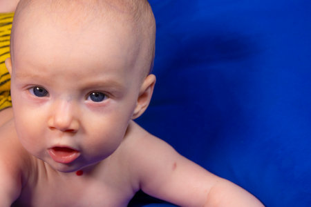 a baby in a tiger diaper on a blue background with a wooden rattleの写真素材