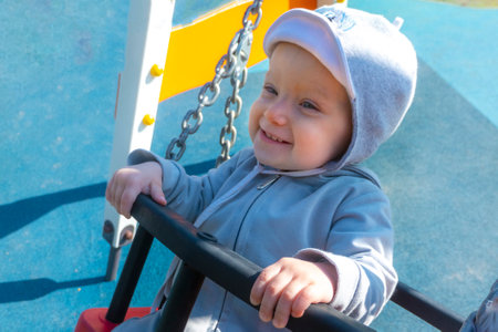 Little girl in sunglasses sits on a rope swing at the playground.の写真素材