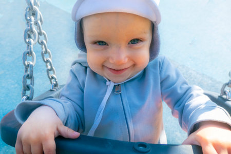 Little girl in sunglasses sits on a rope swing at the playground.の写真素材