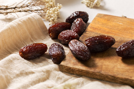 Fresh Medjool dates on a wooden board with linen cloth and dried flowers, highlighting their dark...