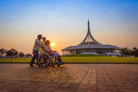 BANGKOK,THAIL AND-FEBRUARY 19  Son and daughter take her mother on wheel chair for exercise and walking for relax with warm light at Suanluang R  9 garden on February 19,2014 in Bangkok,Thailand のeditorial素材