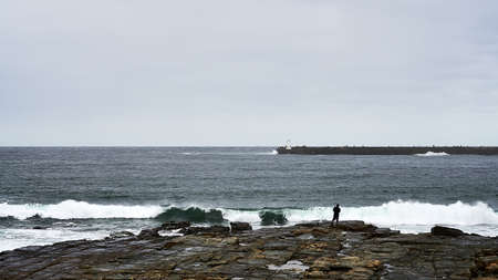 Man fishing on rocks with crashing wavesのeditorial素材