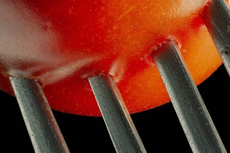 Fork with cherry tomato close-up. Isolated image on a black background. Macro photo.の写真素材