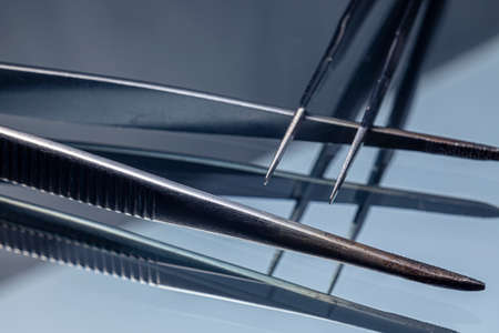 A closeup of two tweezers on a mirrored surface. Tweezers macro photo.の素材 [FY310168249202]