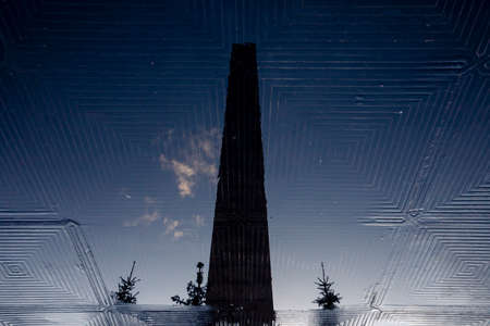 Stone obelisk of the monument to the Heroic Defenders of Leningrad in the reflection of a puddle.の写真素材