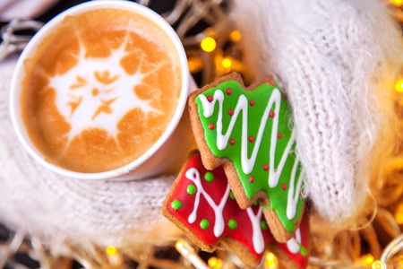 Coffee and Christmas cookies in his hands in the mittens on a background of lightsの写真素材