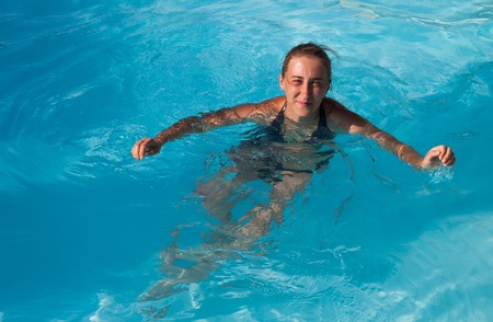 The young beautiful girl floating in the pool with blue waterの写真素材