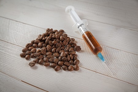 syringe with brown liquid near a handful of coffee beansの写真素材