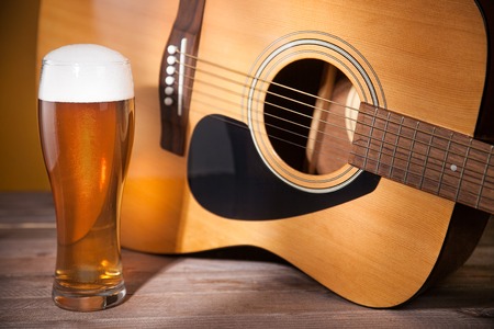 glass of beer with froth near acoustic guitar on wooden table.の写真素材