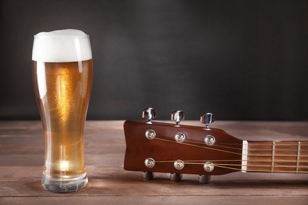 glass of beer next to guitar fretboard on wooden table.の写真素材