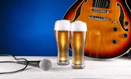 Two glass beer and microphone near electric jazz guitar on white wooden desk. Blue background. Free space for text. Designの写真素材