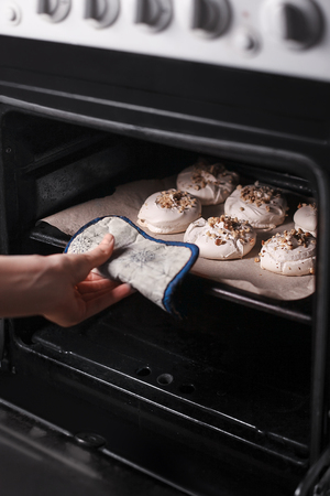 woman's hand pulls out meringue with walnuts  on baker paper from oven. close-up.の写真素材