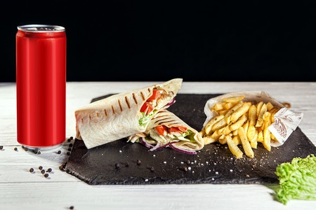 two half sliced shawarma and fri on black slate board next to drink in red aluminum can of 330 ml. Free space for text.の写真素材