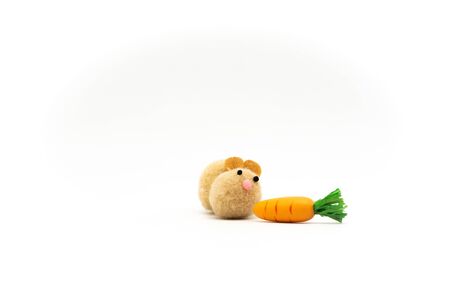 Cute brown pom pom rabbit toy looking at orange carrotの写真素材