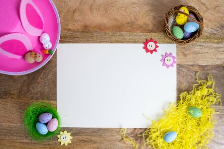 Colorful easter background flat lay on wooden table with white paper space for words. Pink hat,...