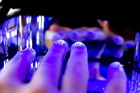 Close up of gel nail polish on short nails curing under UV lightの写真素材