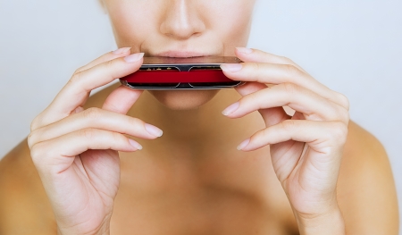 A beautiful young woman is playing harmonica, close-up の写真素材