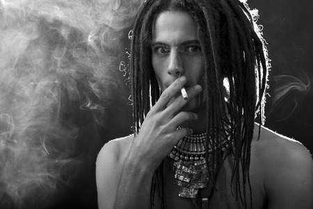 Young man's portrait. Stylish handsome guy with dreadlocks and a cigarette and a variety of stylish silver jewelry dreadlocks and  - Close-up face の写真素材