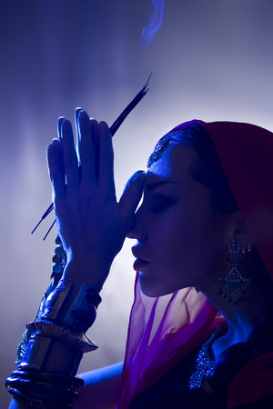 Beautiful young indian woman in traditional clothing with incense and oriental jewelry. Beautiful Girl praying (blue lens effect)の写真素材